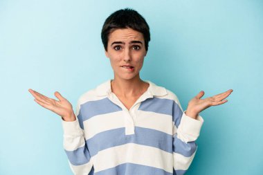 Kafkasyalı genç bir kadın mavi arka planda izole edilmiş. Kafası karışmış ve omuz silkiyor. Kopya alanını tutmak için..