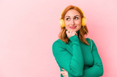 Pembe arka planda izole edilmiş müzik dinleyen beyaz bir kadın şüpheli ve şüpheci bir ifadeyle yana bakıyor..