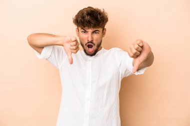 Young arab man isolated on beige background showing thumb down and expressing dislike.