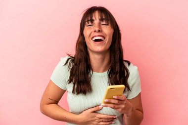 Arjantinli genç bir kadın cep telefonunu pembe arka planda izole edip gülüyor ve eğleniyor..