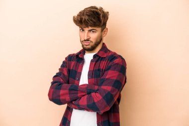 Young arab man isolated on beige background frowning face in displeasure, keeps arms folded.