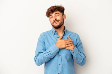 Gri arka planda izole edilmiş genç melez adam, avuçlarını göğsüne bastıran dostane bir ifadeye sahiptir. Aşk konsepti.