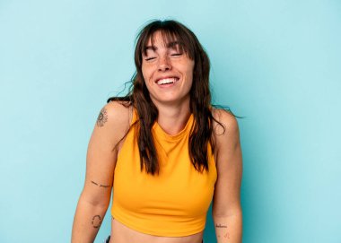 Arjantinli genç bir kadın mavi arka planda izole edilmiş, güler ve gözlerini kapatır, rahat ve mutlu hisseder..