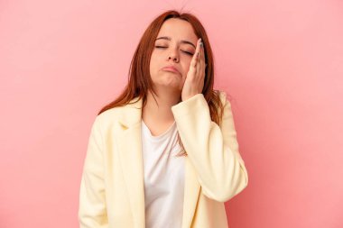 Pembe arka planda izole edilmiş genç beyaz kadın yorgun ve uykulu ellerini başının üstünde tutuyor..