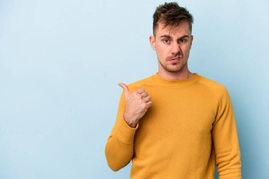 Mavi arka planda izole edilmiş genç beyaz adam işaret parmağıyla fotokopi alanını işaret ederek şok oldu..