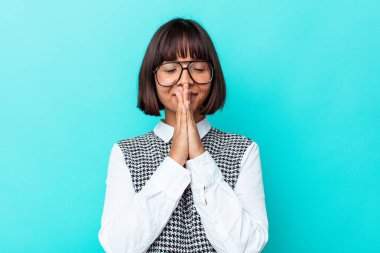 Mavi arka planda izole edilmiş genç melez bir kadın. El ele tutuşup dua ediyor. Kendine güveniyor..