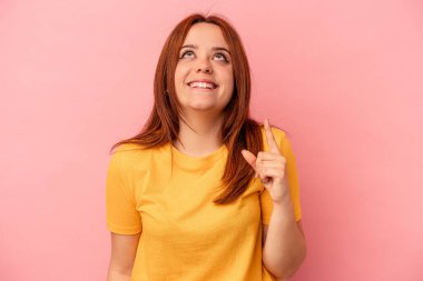 Pembe arka planda izole edilmiş genç beyaz kadın iki parmağı da boş bir alan gösteriyor..