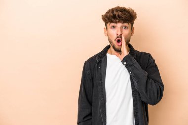 Young arab man isolated on beige background is saying a secret hot braking news and looking aside