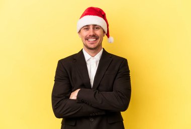 Yeni yılı kutlayan beyaz bir genç adam sarı arka planda izole edilmiş bir Noel şapkası takıyor.