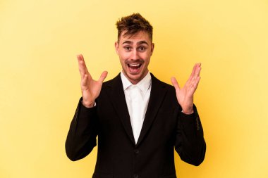 Kafkasyalı genç iş adamı sarı arka planda izole edilmiş hoş bir sürpriz alıyor, heyecanlı ve el kaldırıyor..