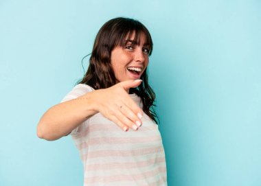 Arjantinli genç bir kadın, mavi arka planda izole edilmiş, elini kameraya uzatarak selam veriyor..