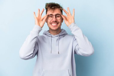 Kafkasyalı genç adam mavi arka planda izole edildi. Heyecanlı görünüyor..