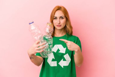 Young caucasian woman recycled plastic isolated on pink background