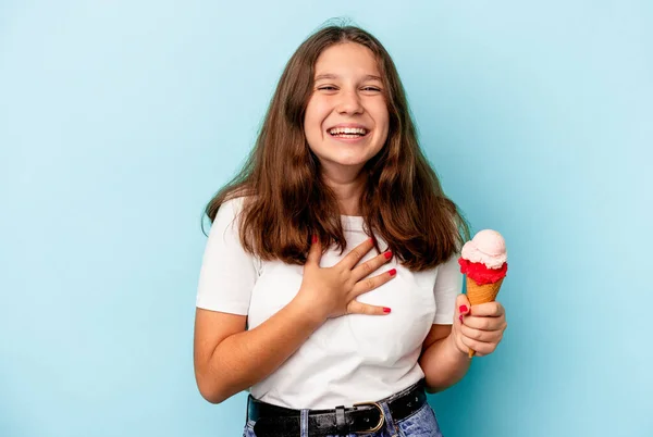 吃着蓝色背景的冰淇淋的白人小女孩大声笑着把手放在胸前 — 图库照片