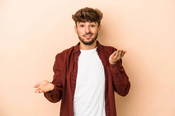Young Arab Man Isolated Beige Background Makes Scale Arms Feels — Stockfoto