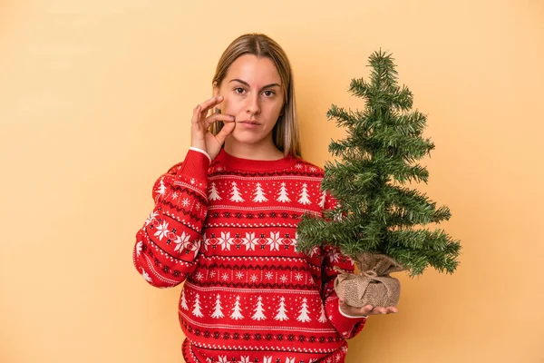 Sarı Arka Planda Izole Edilmiş Küçük Bir Noel Ağacı Tutan — Stok fotoğraf