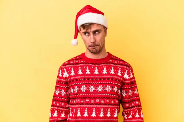 黄色の背景に孤立したクリスマスを祝う若い白人男性混乱し 疑いと不確定な感じ — ストック写真