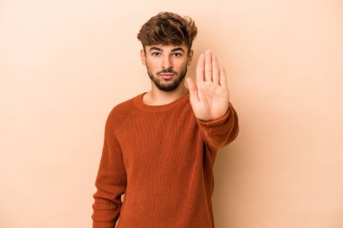 Young arab man isolated on beige background standing with outstretched hand showing stop sign, preventing you.
