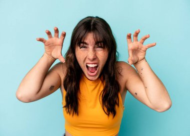 Arjantinli genç bir kadın mavi arka planda, pençelerini kedi taklidi yaparken gösteriyor, agresif bir hareket..