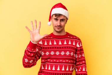 Sarı arka planda izole edilmiş, beş numarayı parmaklarıyla gülümseyerek kutlayan Kafkasyalı genç adam..