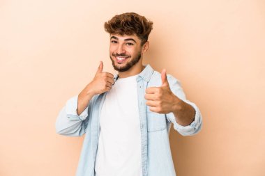 Young arab man isolated on beige background raising both thumbs up, smiling and confident.