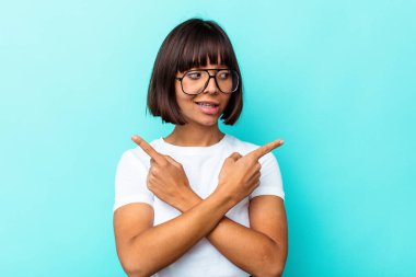 Mavi arka plan noktalarında izole edilmiş genç melez kadın iki seçenek arasında seçim yapmaya çalışıyor..