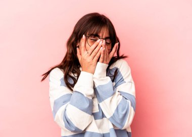 Arjantinli genç bir kadın pembe arka planda izole edilmiş parmaklarıyla kameraya göz kırpıyor, yüzünü kapatmaktan utanıyor..