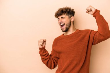 Young arab man isolated on beige background raising fist after a victory, winner concept.