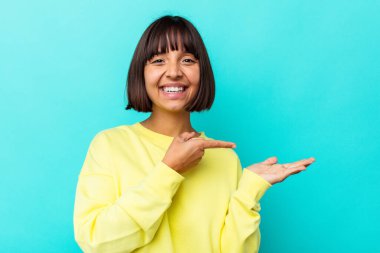 Mavi arka planda izole edilmiş genç melez bir kadın. Elinde bir kopya tutarken heyecanlanıyor..