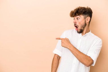 Young arab man isolated on beige background points with thumb finger away, laughing and carefree.