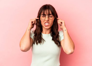 Arjantinli genç bir kadın pembe arka planda izole edilmiş parmaklarıyla kulaklarını kapatıyor, gürültülü bir ortam yüzünden stresli ve çaresiz..