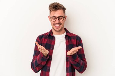 Beyaz arka planda izole edilmiş genç beyaz bir adam elinde avuç içi bir şeyle kameraya sunuyor..