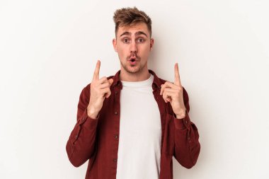 Beyaz arka planda izole edilmiş genç beyaz adam ağzı açık bir şekilde üst tarafı işaret ediyor..