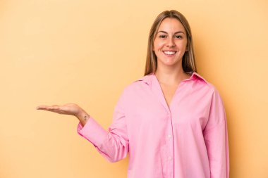 Sarı arka planda izole edilmiş genç beyaz kadın bir avuç içinde fotokopi alanı ve belinde bir el daha gösteriyor..