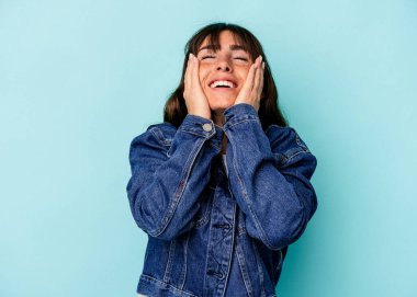 Mavi arka planda izole edilmiş genç Arjantinli kadın mutlu bir şekilde ellerini başının üstünde tutuyor. Mutluluk kavramı.