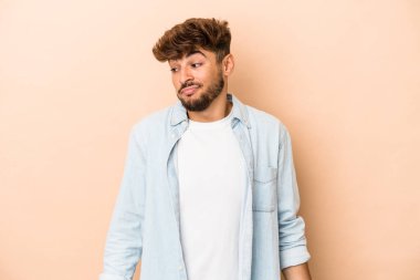 Young arab man isolated on beige background shrugs shoulders and open eyes confused.