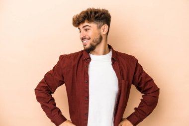 Young arab man isolated on beige background confident keeping hands on hips.