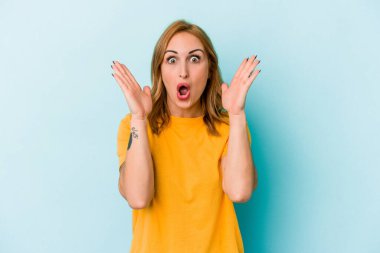 Mavi arka planda izole edilmiş genç beyaz kadın şaşırdı ve şok oldu..