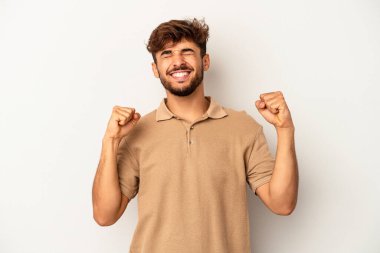 Genç melez adam gri arka planda izole edilmiş zaferi, tutkuyu ve coşkuyu kutluyor, mutlu bir ifade..
