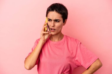 Pembe arka planda cep telefonu tutan beyaz bir kadın.