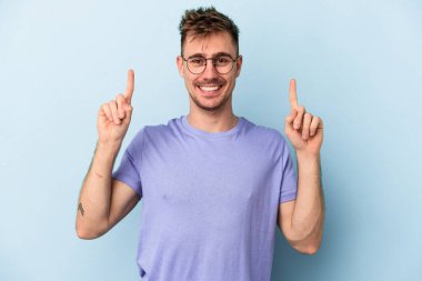 Mavi arka planda izole genç beyaz adam işaret iki ön parmakları boş bir boşluk gösteren.