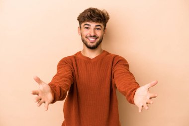 Young arab man isolated on beige background showing a welcome expression.