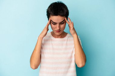 Mavi arka planda izole edilmiş genç beyaz kadın şakaklara dokunuyor ve baş ağrısı çekiyor..