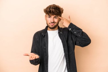 Young arab man isolated on beige background holding and showing a product on hand.