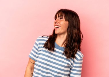 Arjantinli genç bir kadın pembe arka planda izole edilmiş rahat ve mutlu bir şekilde gülüyor, boynunda dişlerini gösteriyor..