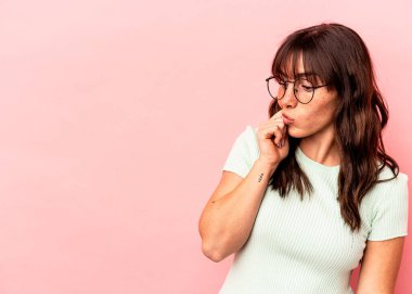 Pembe arka planda izole edilmiş genç Arjantinli kadın şüpheli ve şüpheci bir ifadeyle yana bakıyor..