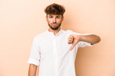 Young arab man isolated on beige background showing a dislike gesture, thumbs down. Disagreement concept.