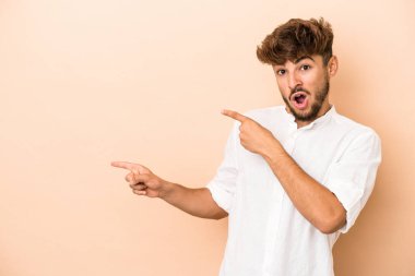 Young arab man isolated on beige background pointing with forefingers to a copy space, expressing excitement and desire.