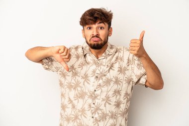 Genç melez adam gri arka planda izole edilmiş, baş parmağını kaldırıyor, zor seçim konsepti.