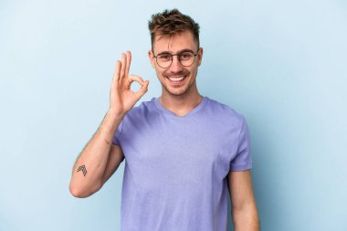 Kafkasyalı genç adam mavi arka planda izole edilmiş neşeli ve kendinden emin..